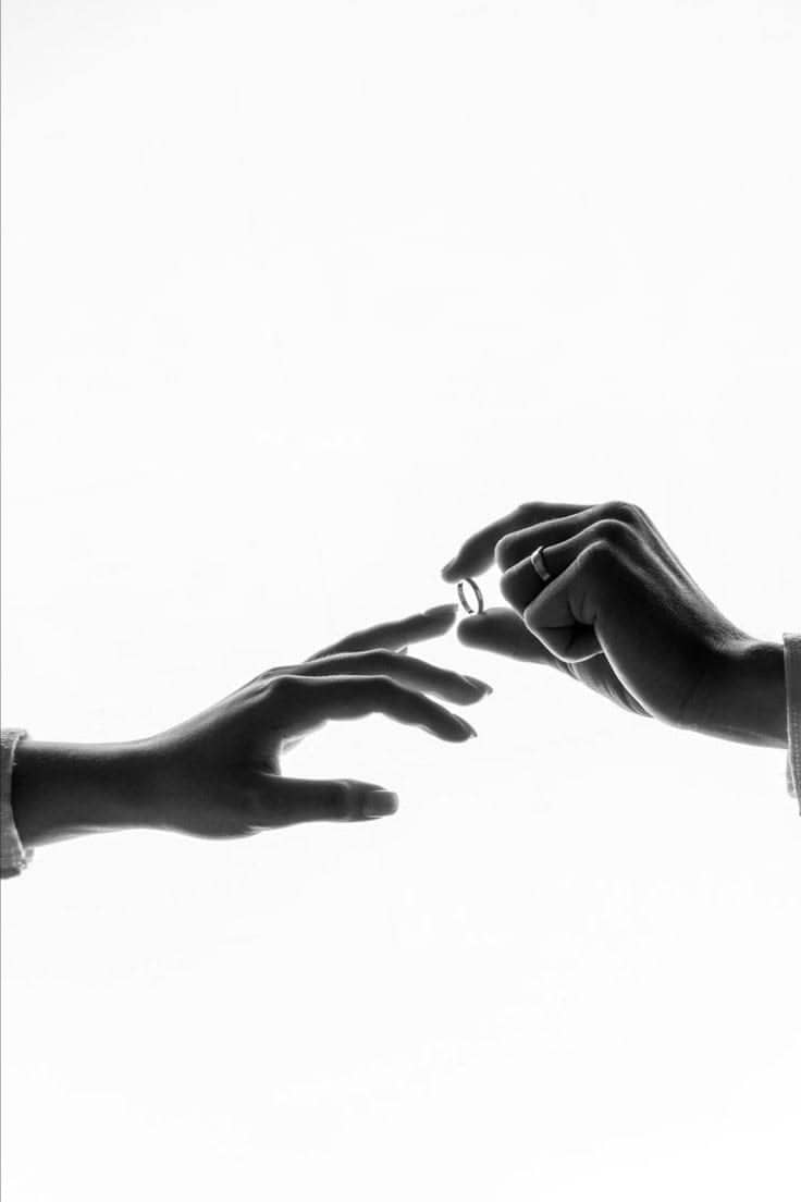 Hands exchanging an engagement ring against soft light