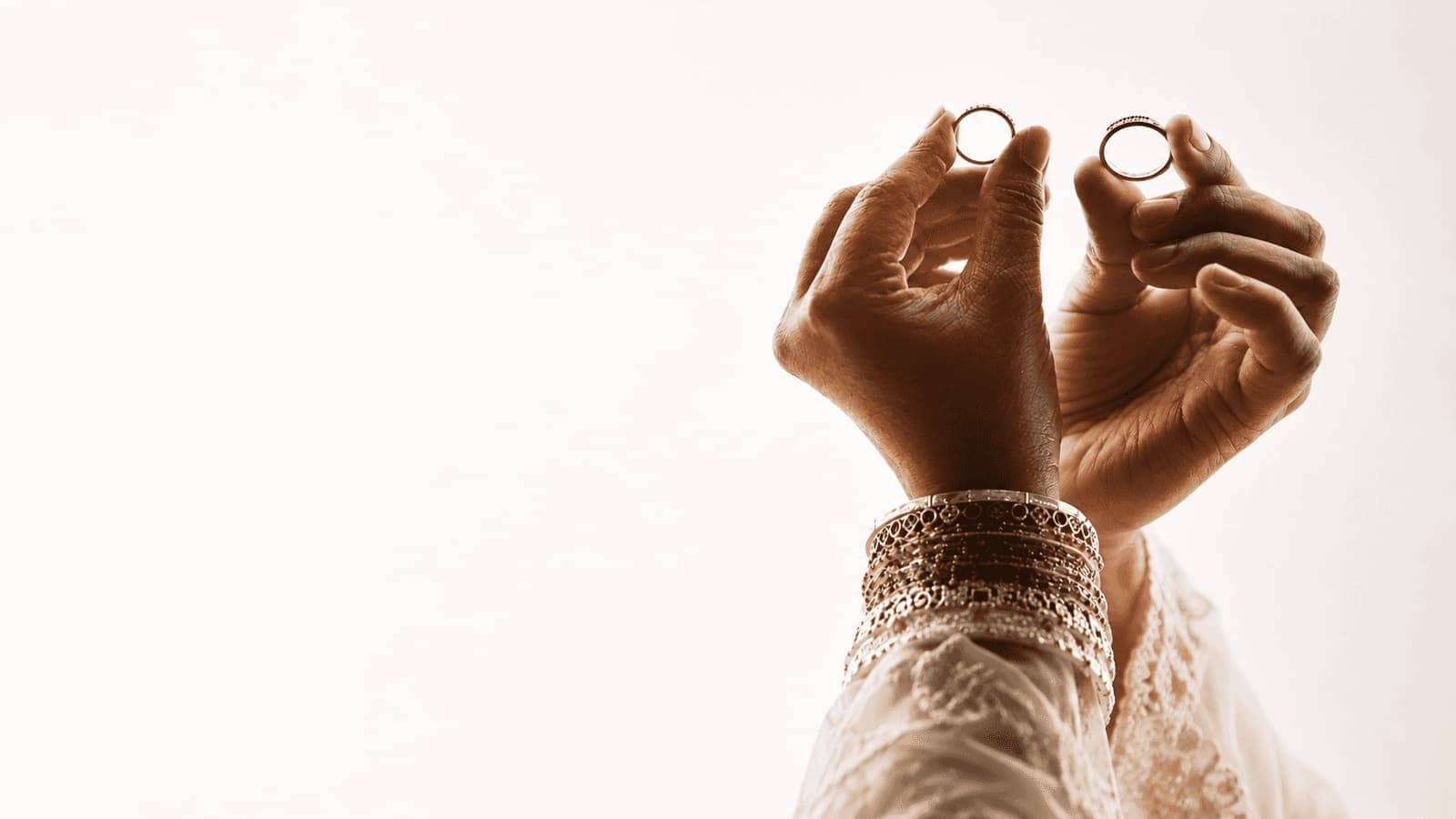 Two hands holding wedding bands toward the light